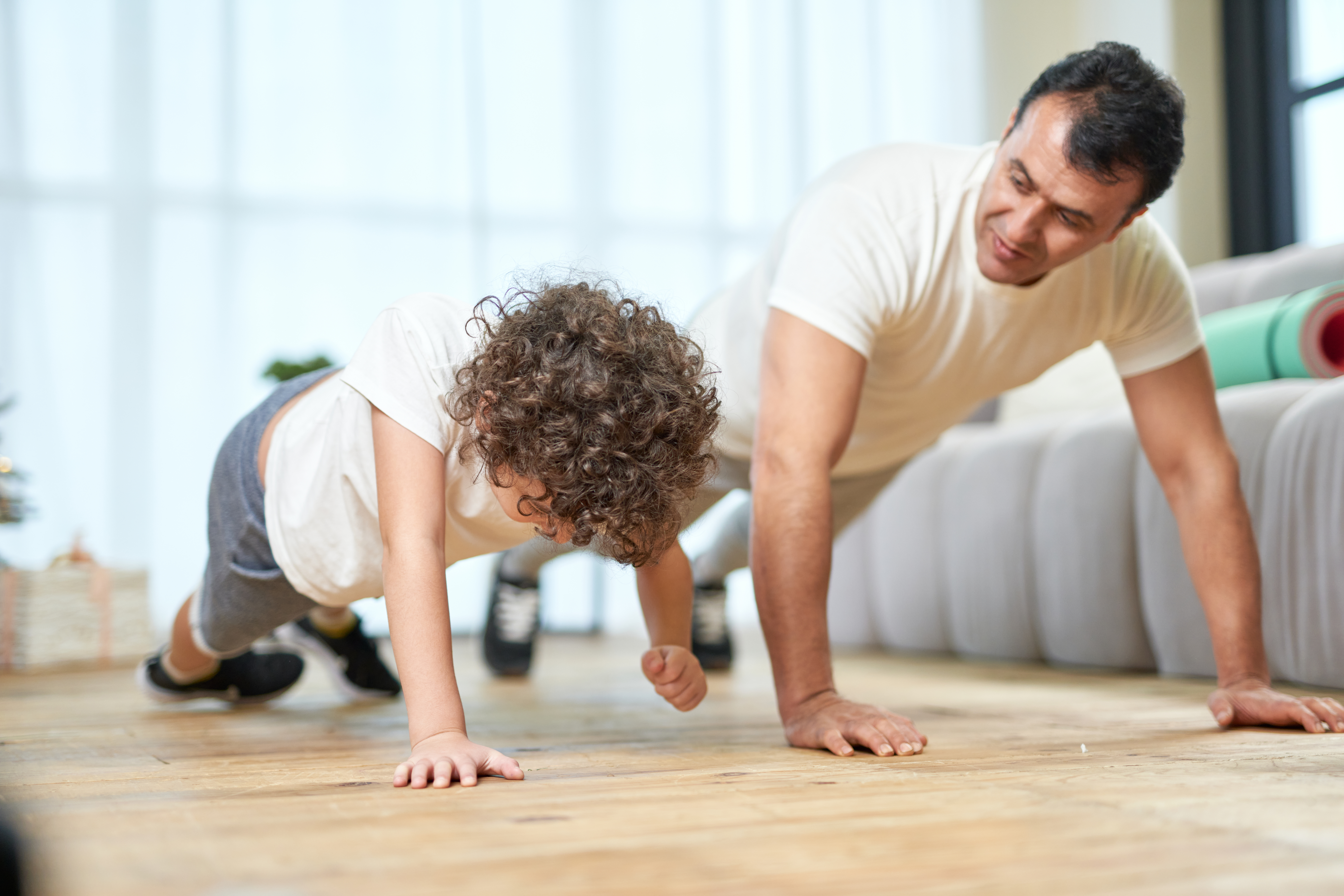 Training at Home. Sportive latin middle aged father teaching his son doing push ups while spending time together at home